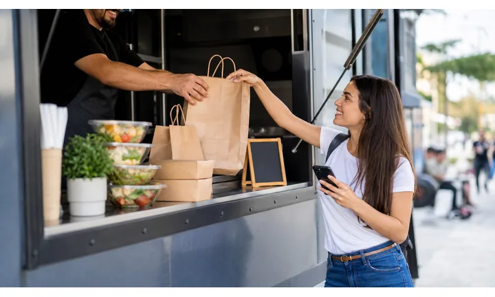 Banco di ritiro del food truck con sacchetti da asporto e smartphone del cliente.